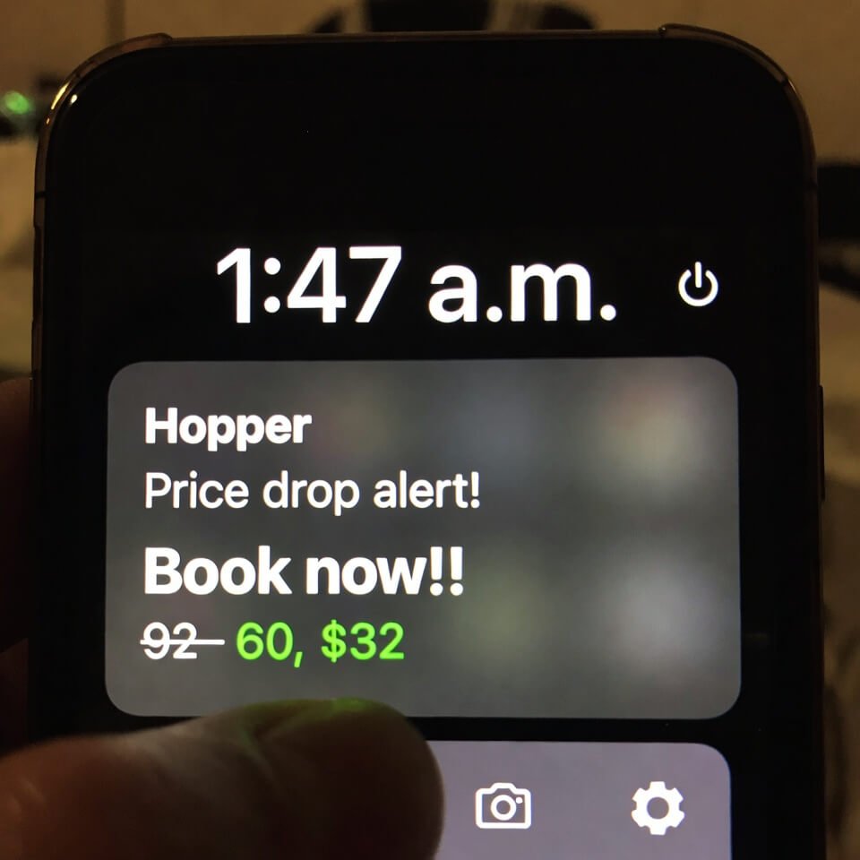 Half-asleep phone at 1:47 a.m. displaying Hopper price drop alert $92 off, thumb covering part of screen
