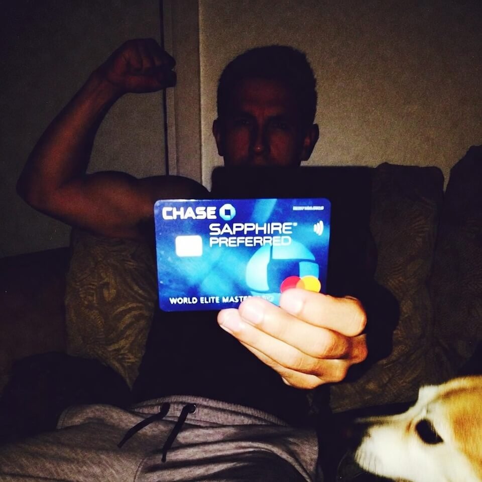 Grainy selfie holding Chase Sapphire Preferred card triumphantly, unimpressed dog photobombed.