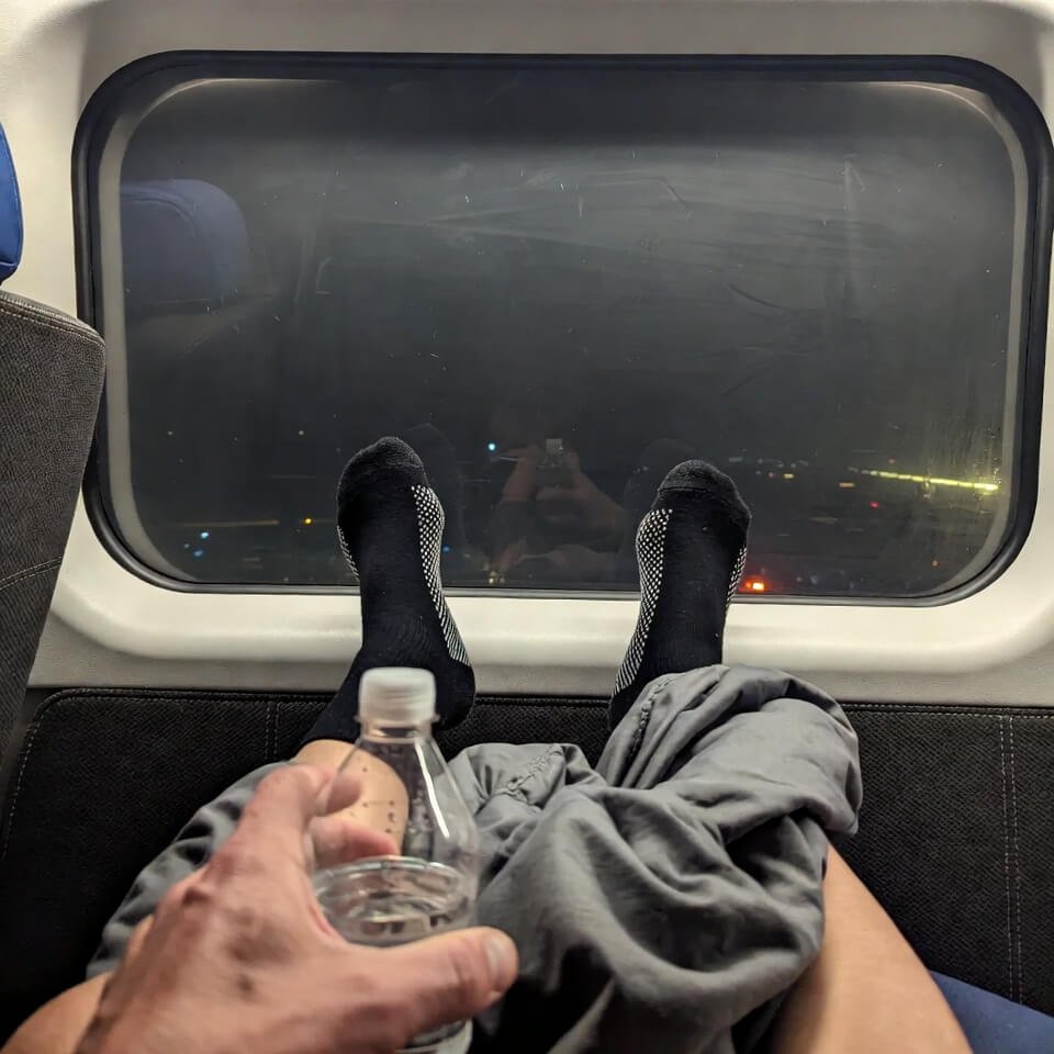 Compression-socked feet propped up, water bottle in hand, night city lights below.