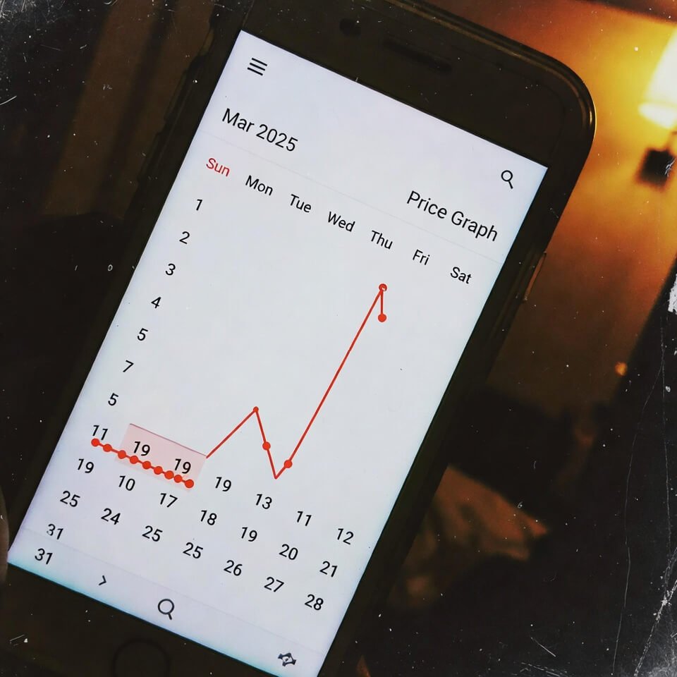 Tilted phone showing Google Flights price graph spiking sharply in dim hotel light.