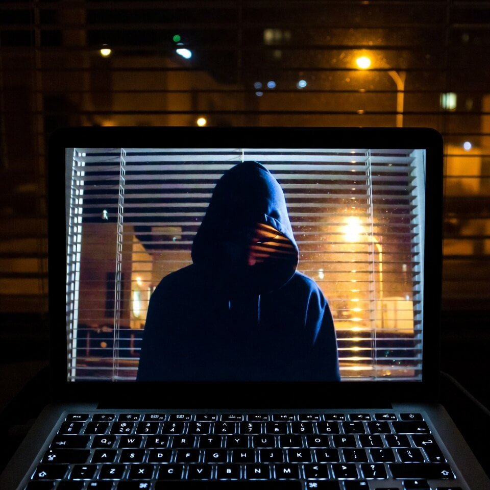 Hooded person reflected in MacBook screen at night